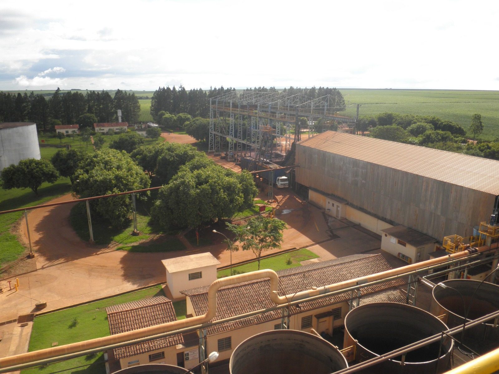 Vista da planta industrial da Destilaria Cachoeira, com esteiras, galpões e canaviais ao fundo em Tupaciguara-MG